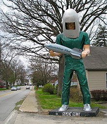 Picture of statue, man in green uniform and helmet holding rocket