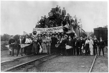 People displaying Chatauqua sign surrounding Railroad engine car